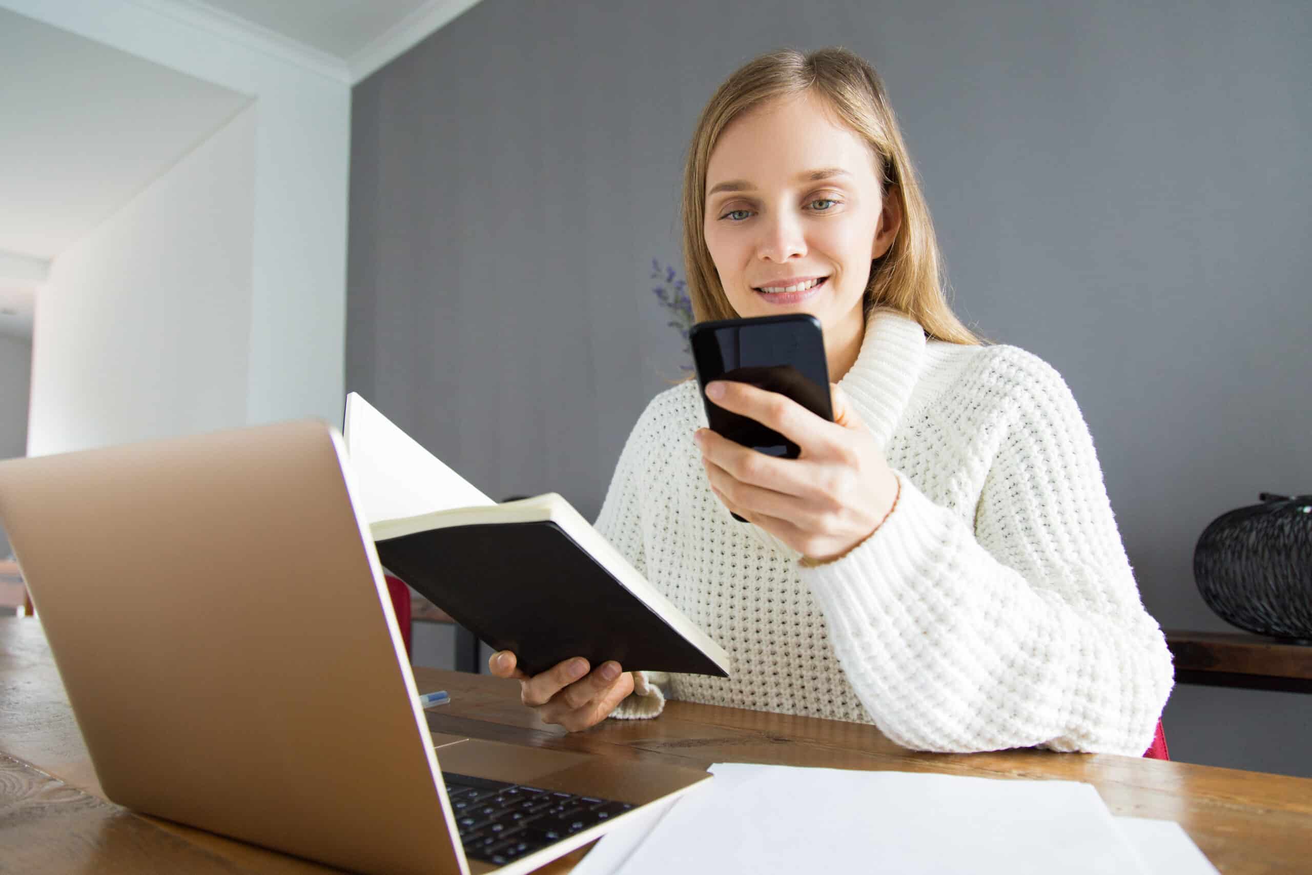 smiling woman holding a phone and a notebook